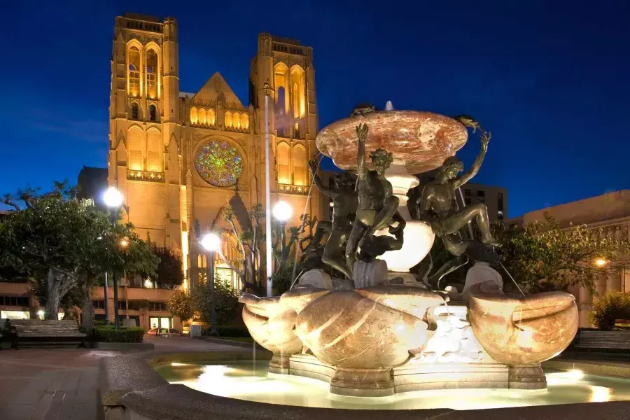 大教堂的恩典 de San Francisco aparece fotografiada de noche con una fuente de agua ornamentada en primer plano.